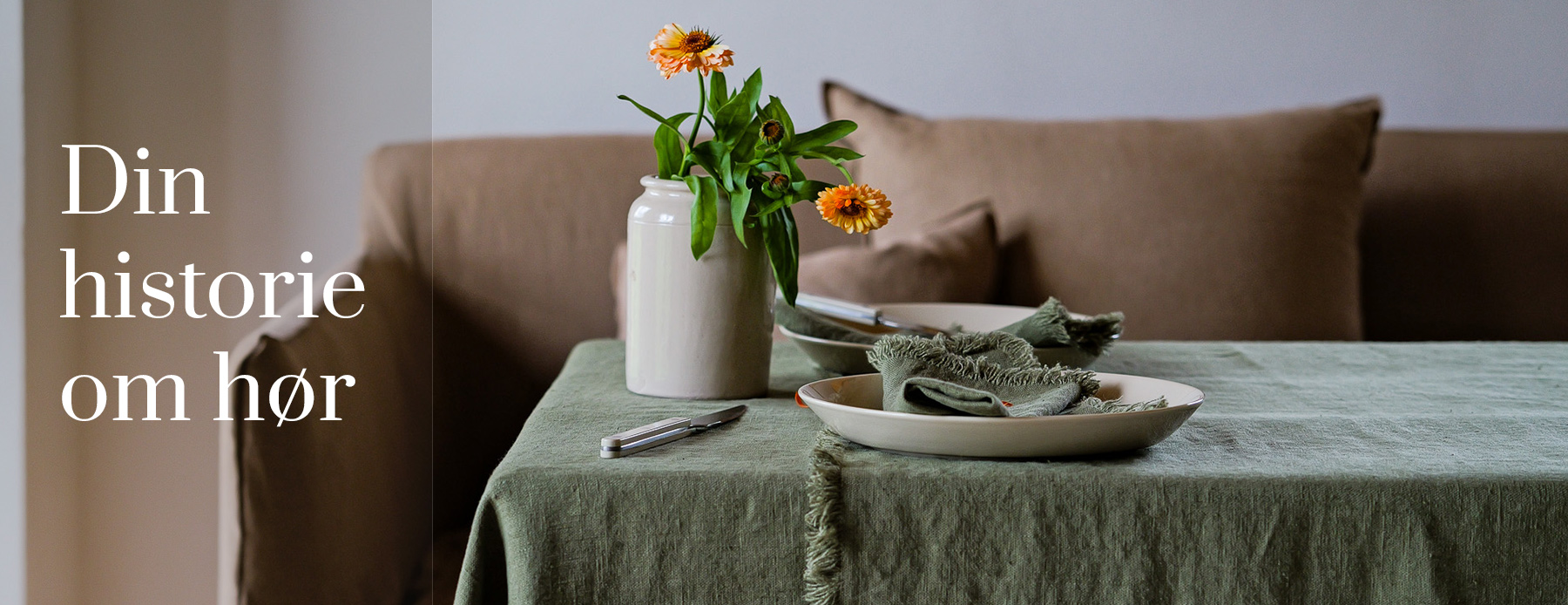 Din historie om hør – grøn hørdug med servietter og efterårsblomster foran en sofa.