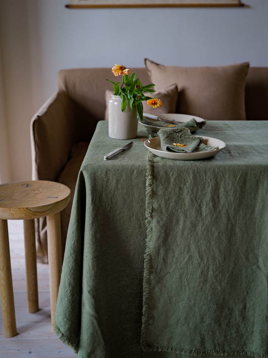 Olivengrøn hørdug med frynser, cremefarvede tallerkener og blomstervase