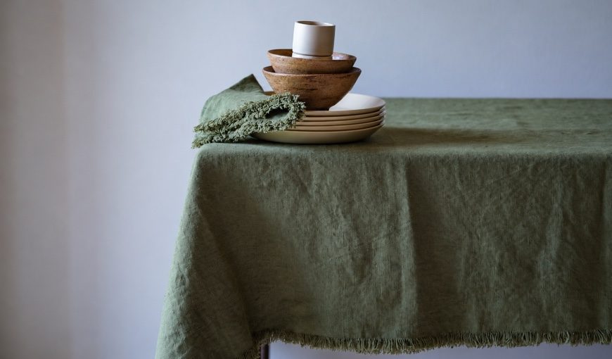 Olive Green Terra Fringe-hørdug og serviet med cremefarvede tallerkener og træskåle